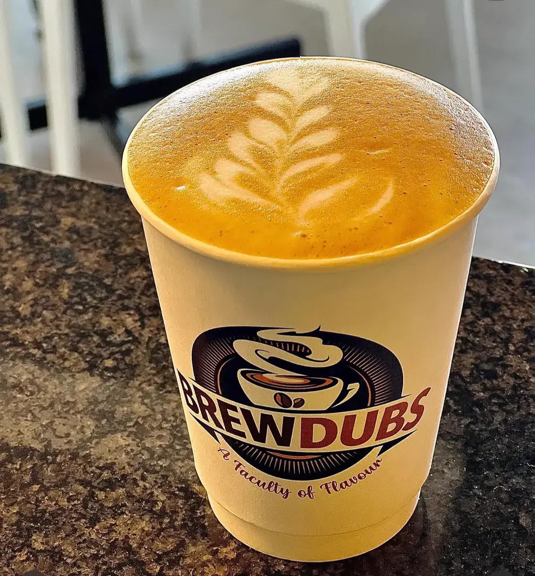 A BrewDubs takeaway cup on the counter, filled with a latte and finished with a leaf pattern in the foam.