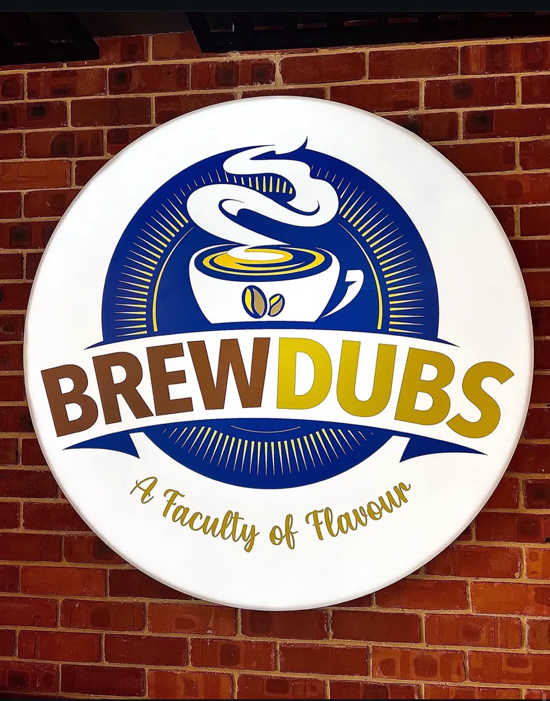 The BrewDubs sign, a circular blue and gold badge, mounted on the red brick wall inside the shop.
