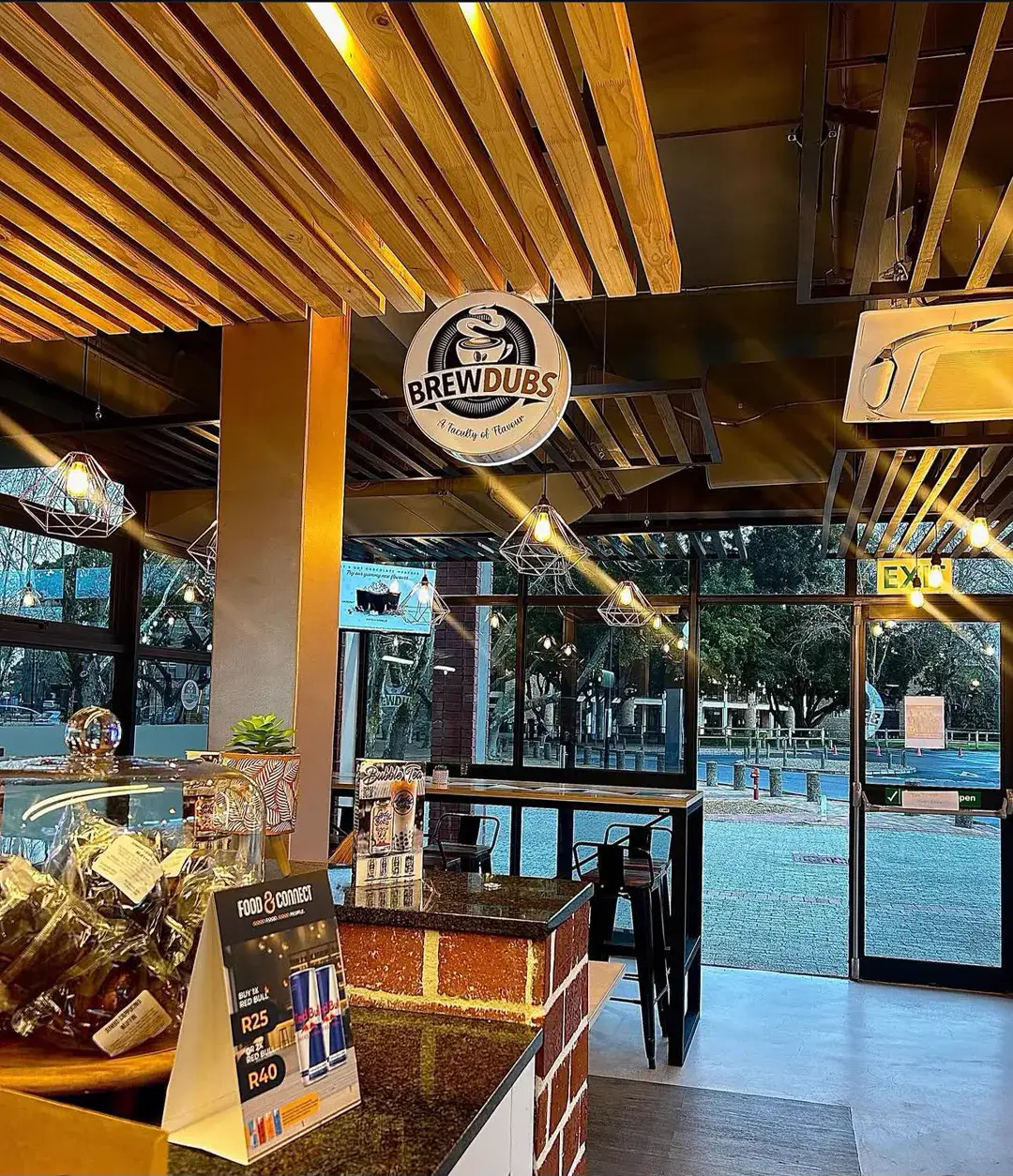 The BrewDubs counter, with the hanging logo sign, timber ceiling slats and filament bulbs above it.
